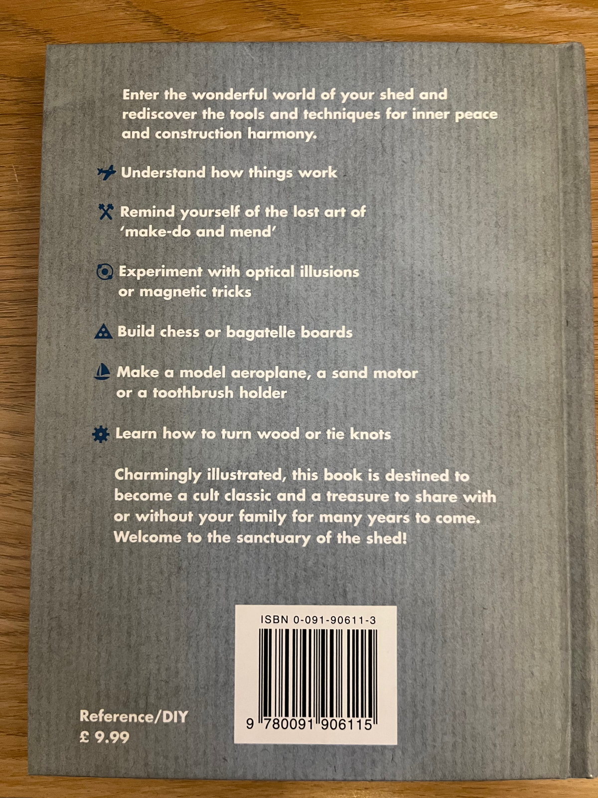 The back cover of a DIY craft book titled 'Enter the wonderful world of your shed and rediscover the tools and techniques for inner peace and construction harmony' by Chris Hinchcliffe, placed on a wooden surface. The cover is gray with white text, a barcode, and a small logo in the top right.