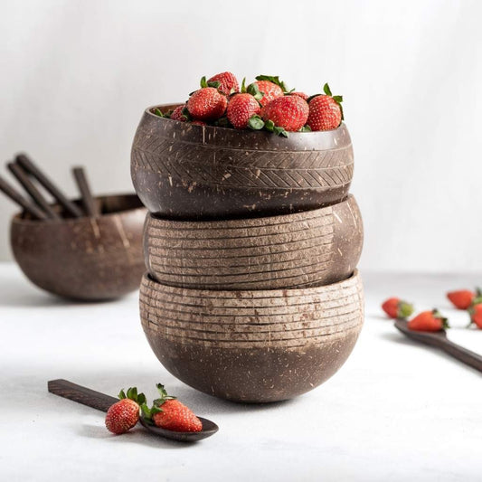 Three coconut bowls with spoons and strawberries