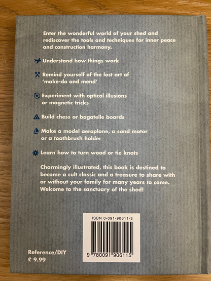 The back cover of a DIY craft book titled 'Enter the wonderful world of your shed and rediscover the tools and techniques for inner peace and construction harmony' by Chris Hinchcliffe, placed on a wooden surface. The cover is gray with white text, a barcode, and a small logo in the top right.